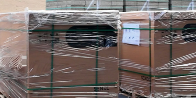 Mehrere auf Paletten gestapelte, in Folie verpackte Kartons mit grünen Umreifungsbändern und Versandetiketten.